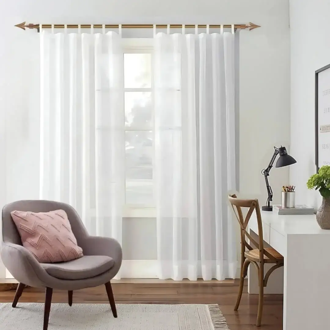 Elegant white sheer curtains gracefully draped over a lustrous gold curtain rod in a chic living room, accented with a stylish chair and table—creating a light, airy, and sophisticated atmosphere